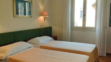 Une chambre d’hôtel avec deux lits, une table de chevet, une lampe, une fenêtre avec des rideaux et un tableau encadré au mur.