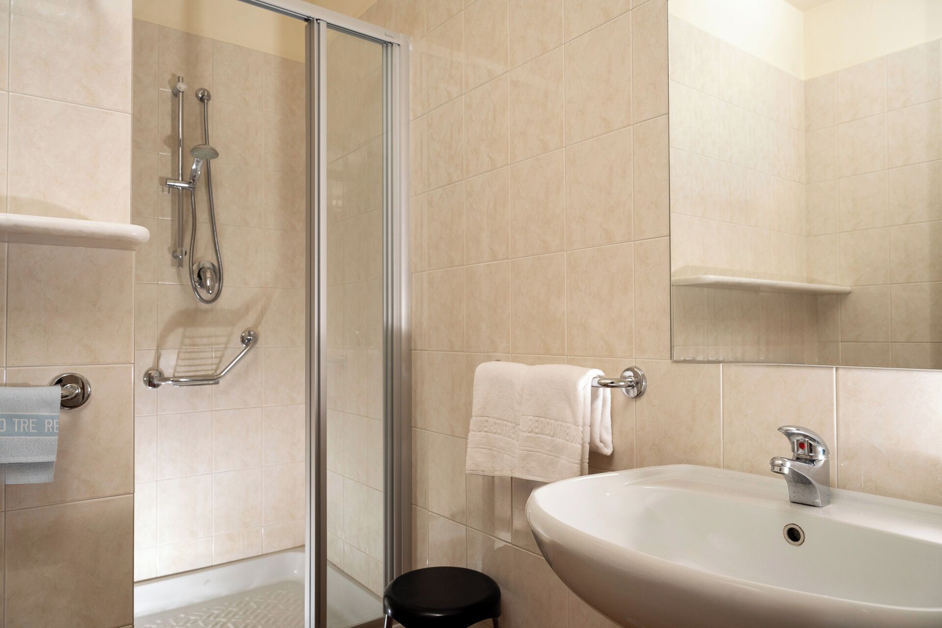 A modern bathroom with a glass shower enclosure, a white sink, and a towel rack.