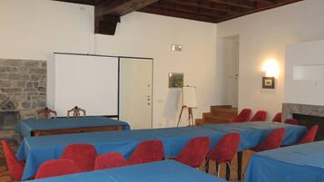 Un salón de conferencias con varias mesas cubiertas con manteles azules y sillas rojas. Hay una pizarra, una chimenea y una pared de piedra.