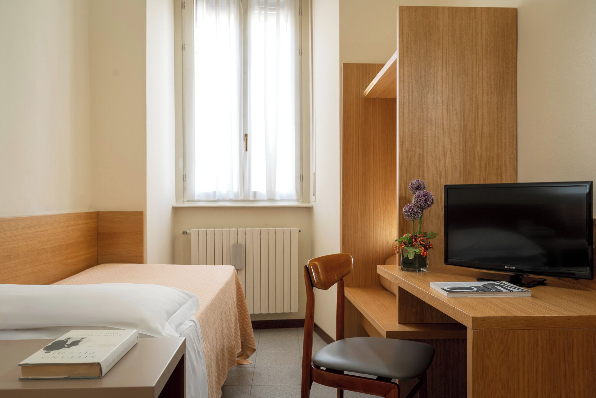 Ein Hotelzimmer mit einem Bett, einem Schreibtisch mit Stuhl, einem Fernseher und einem Fenster mit Vorhängen.