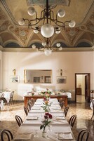 Une salle à manger élégante, avec une longue table dressée pour un repas, un lustre et un plafond décoratif.
