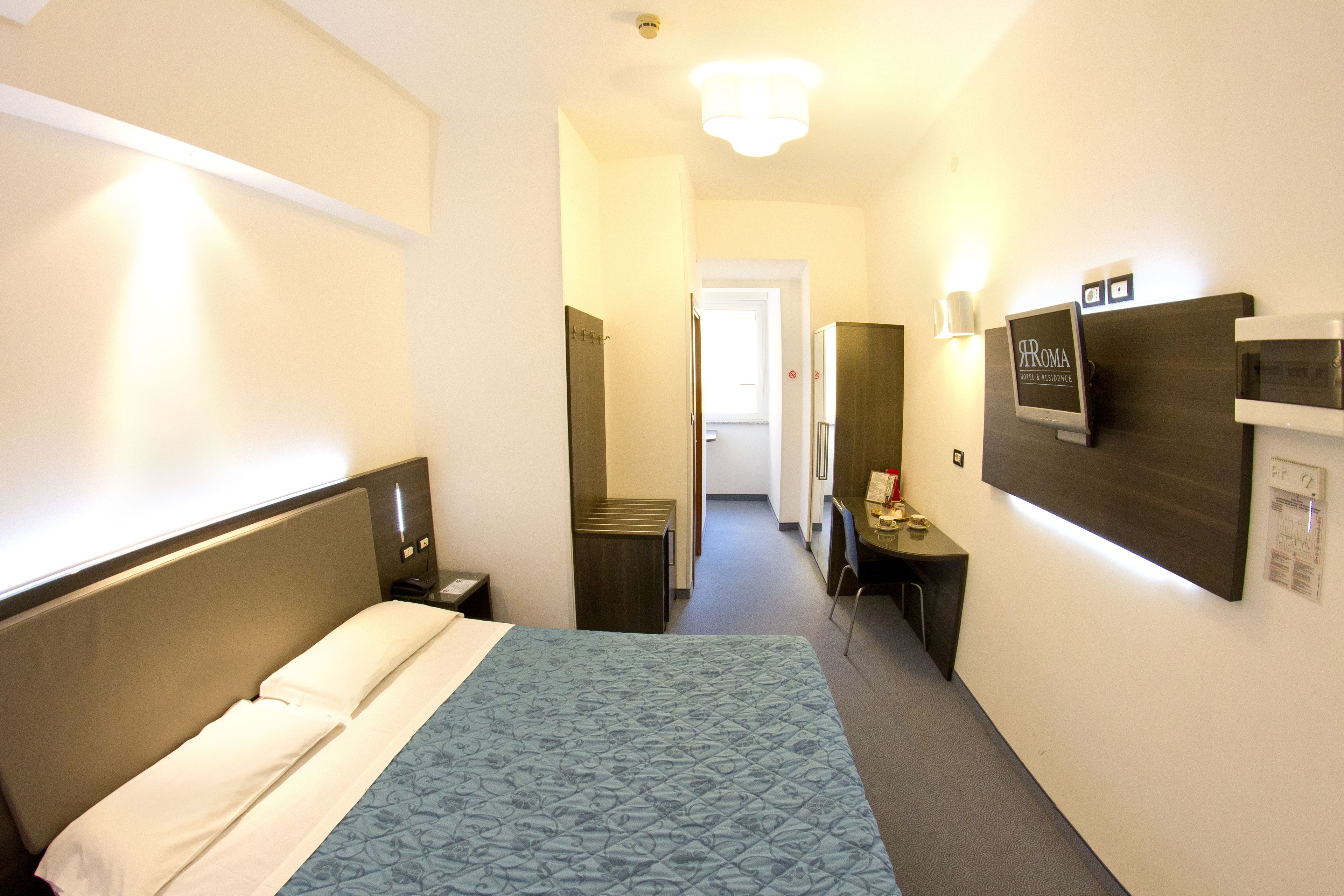 Een hotelkamer met een bed, nachtkastje, lamp en een aan de muur bevestigde televisie.