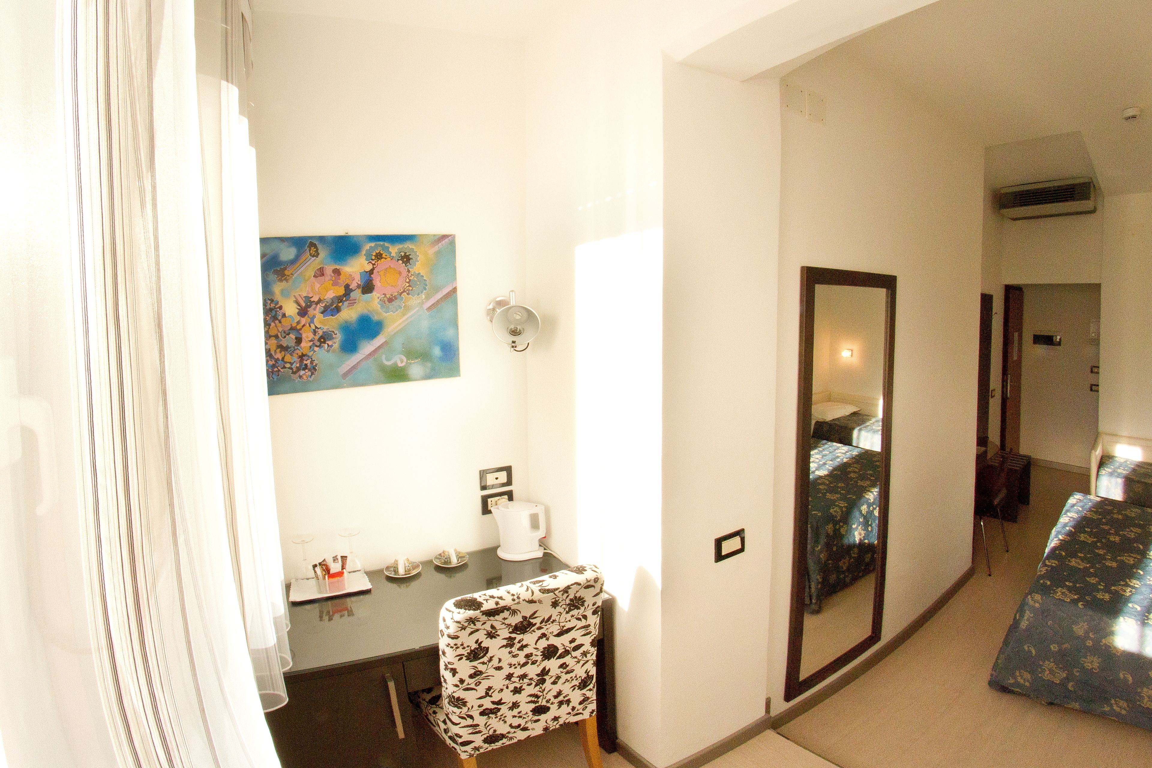 Een hotelkamer met een bed, een bureau, een stoel, een schilderij aan de muur en een spiegel.