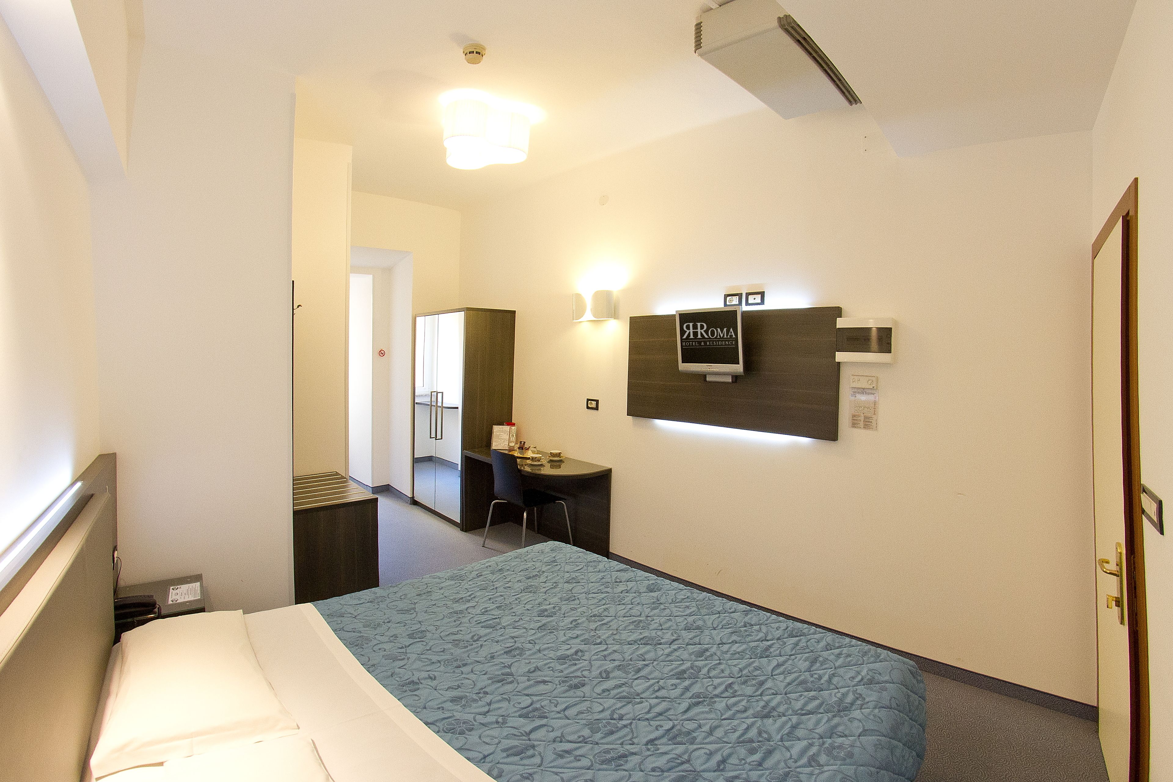 A hotel room with a bed, a desk, a chair, and a mirror.