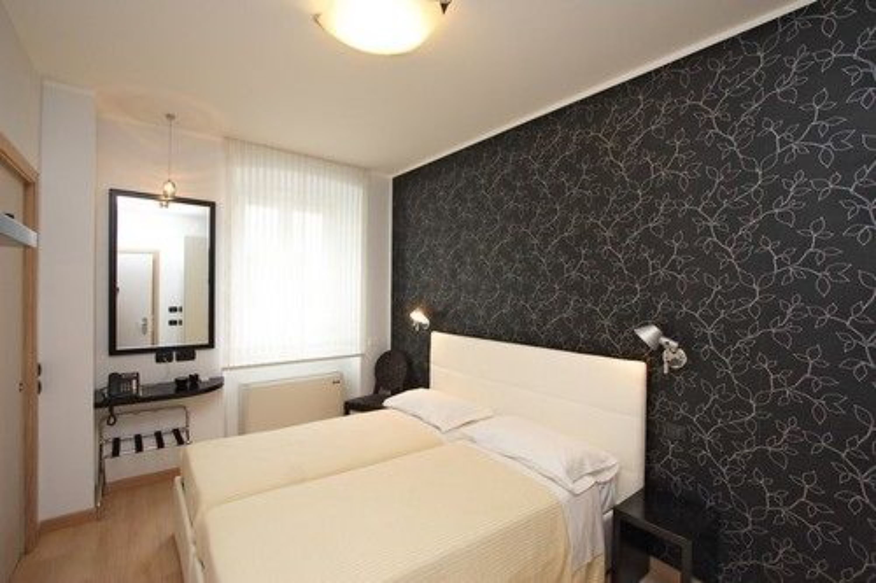 Habitació d'hotel amb llit, taula de nit, làmpada i mirall.