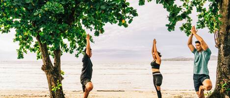 Three people performing yoga on a wooden deck with a view of the sea and trees.