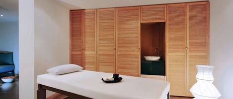 Una habitación con una mesa de masaje, puertas correderas de madera, un cuenco y un florero.