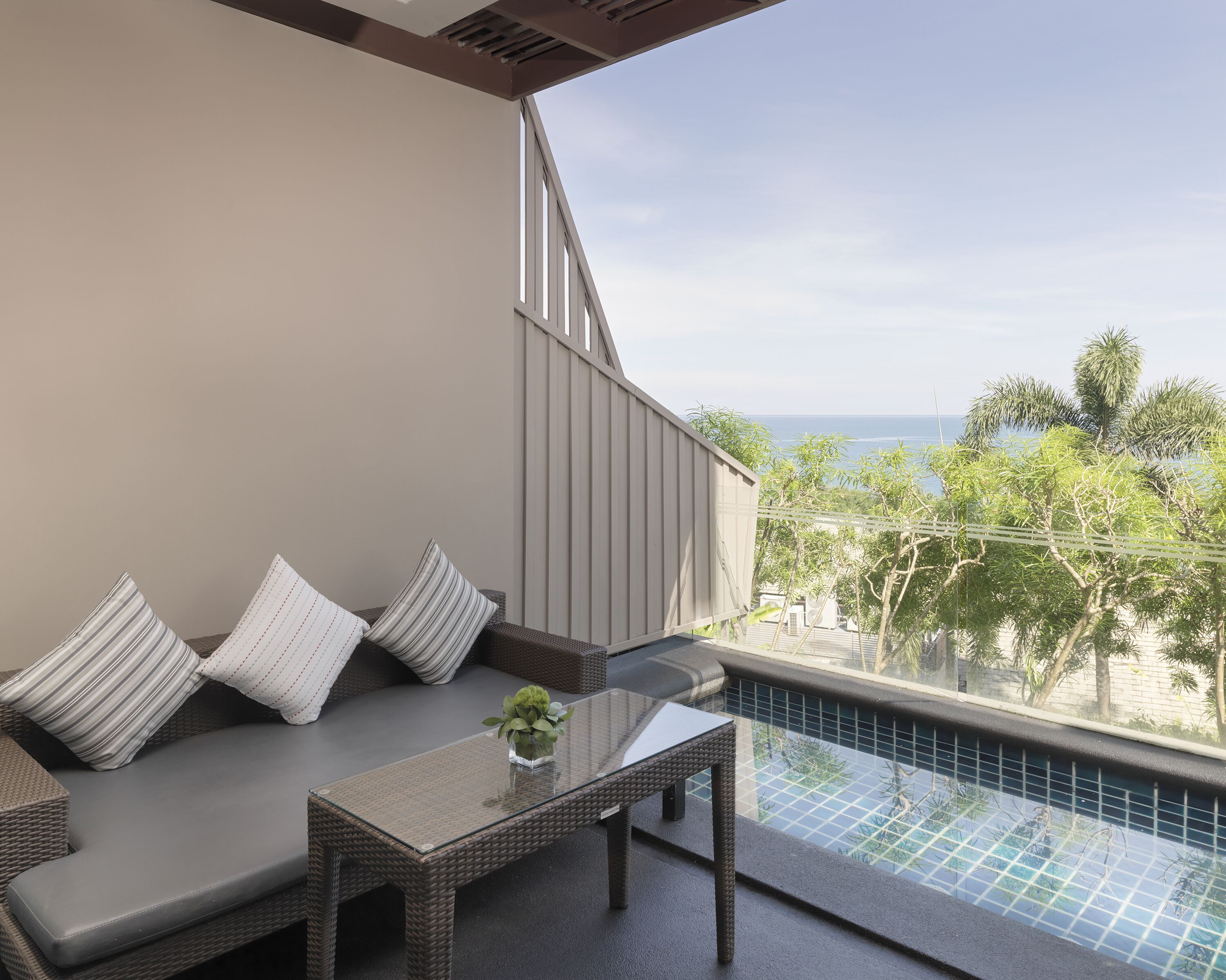A balcony with a glass-top table, wicker sofa, and striped cushions.
