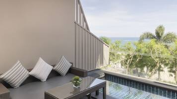 A balcony with a glass-top table, wicker sofa, and striped cushions.