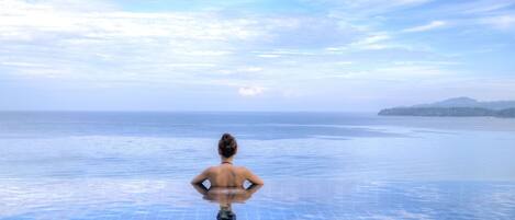 A person standing at the edge of a infinity pool with a view of the sea and distant land.