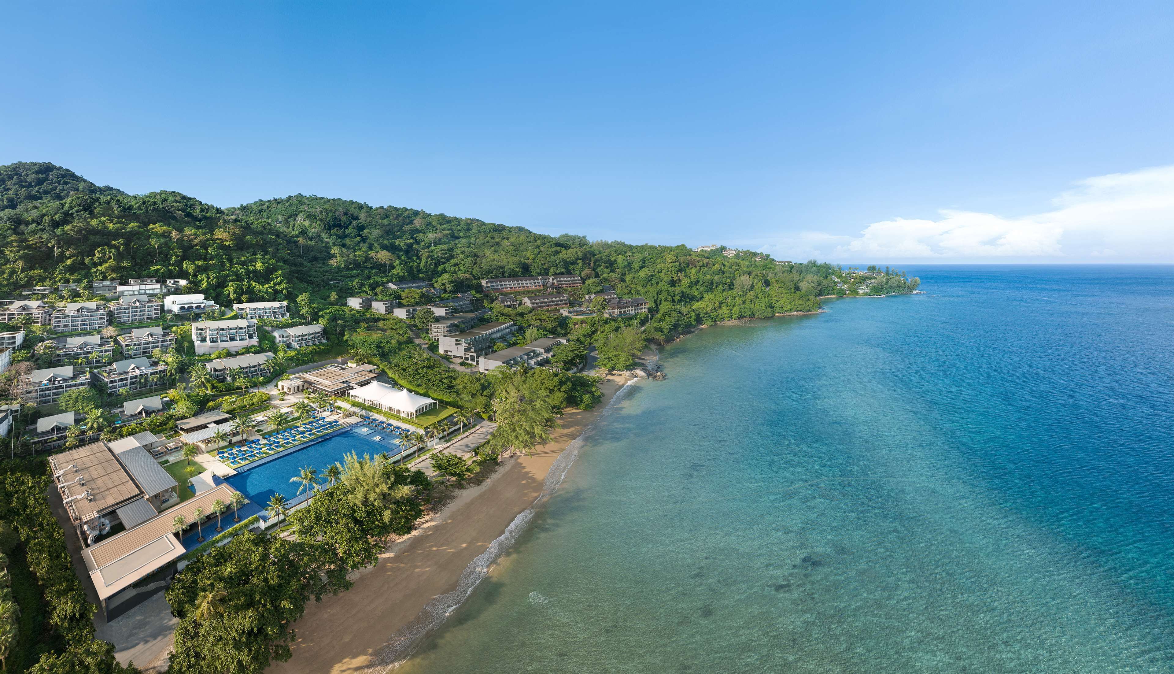 An aerial view of a coastal resort with multiple buildings, a swimming pool, and a beach.