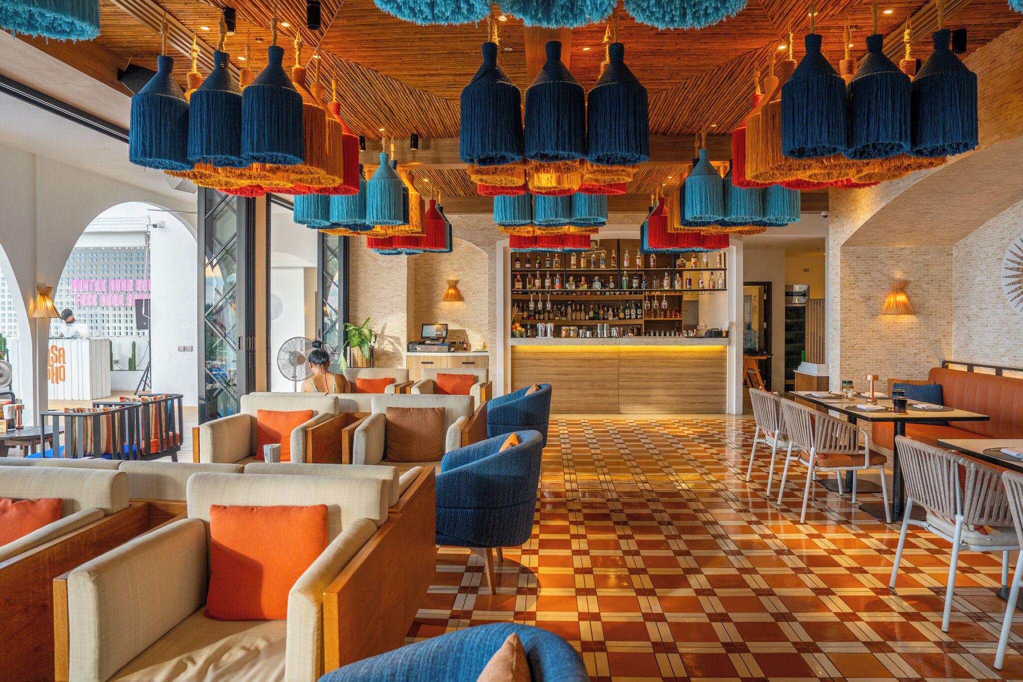 Un área de descanso moderna con asientos azules y anaranjados, suelo a cuadros y un bar al fondo.