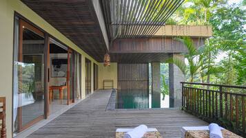 A wooden deck with a pool, wooden furniture, and a view of lush greenery.