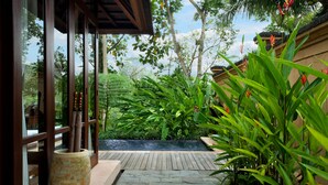 A pathway leading to a wooden deck with a large planter and lush greenery. - Komaneka at Tanggayuda (Ubud)