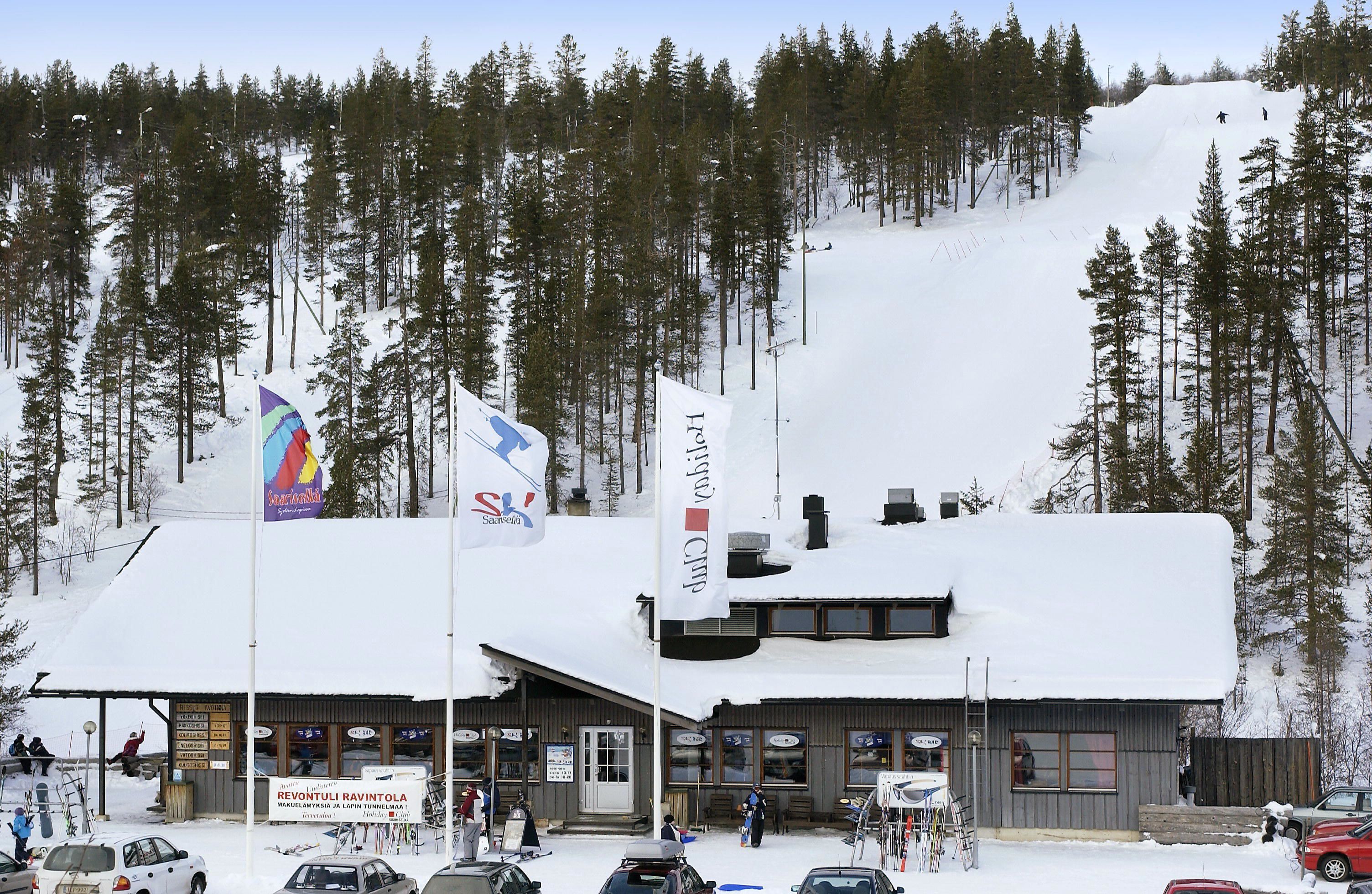 Ein Skigebietsgebäude mit einem Schild für 'Revontuli Ravintola' und einer Skipiste im Hintergrund.