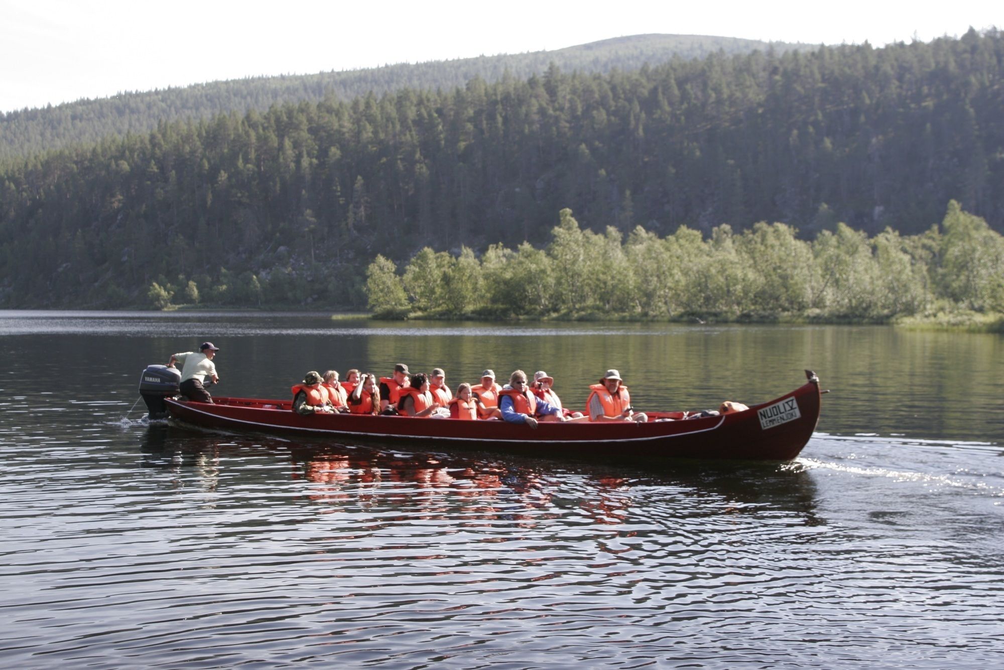 Una canoa amb persones portant armilles salvavides en un llac tranquil envoltat de bosc.