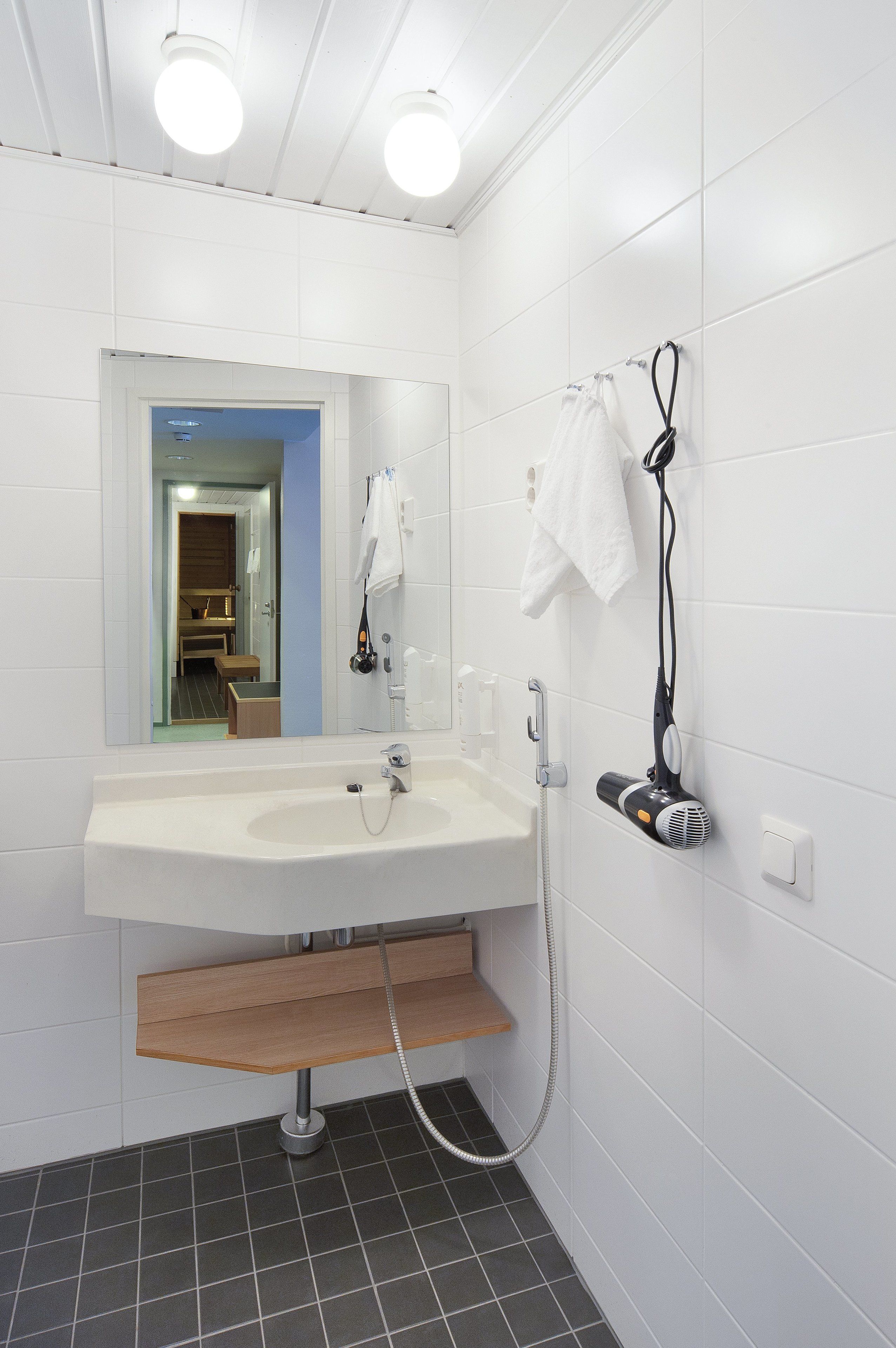 Une salle de bain moderne avec un lavabo blanc, une douchette à main et un sèche-cheveux fixé au mur.