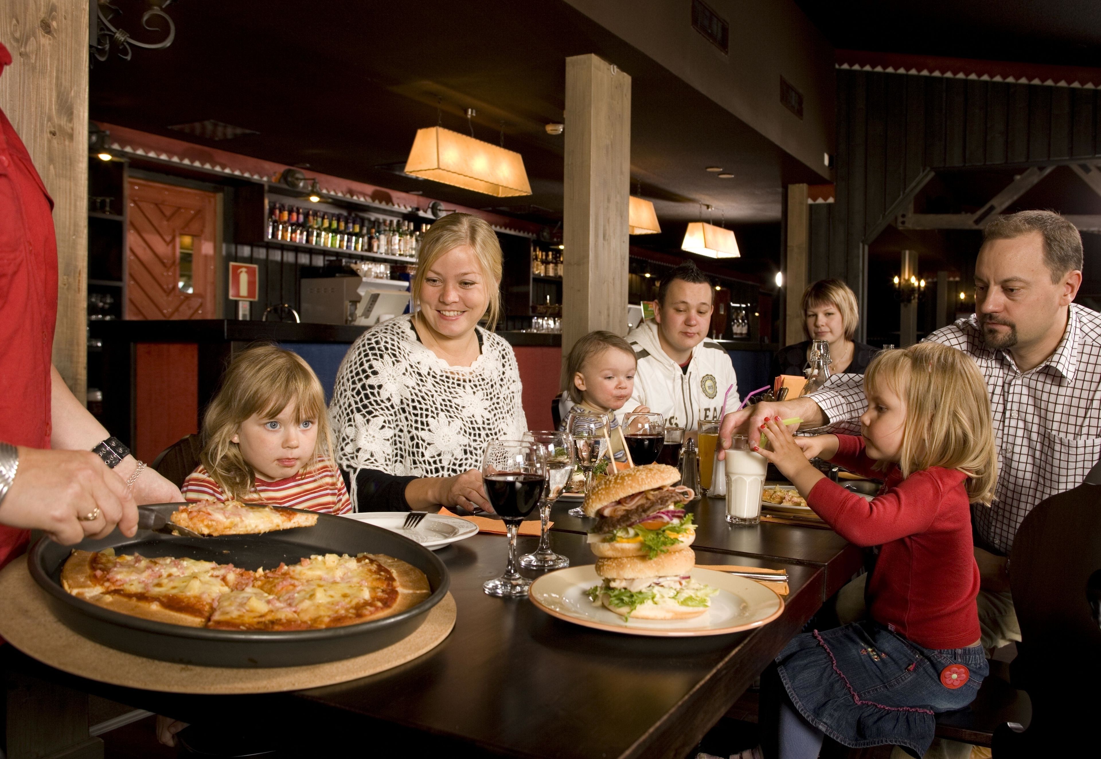A family dining at a restaurant with pizza and burgers on the table.