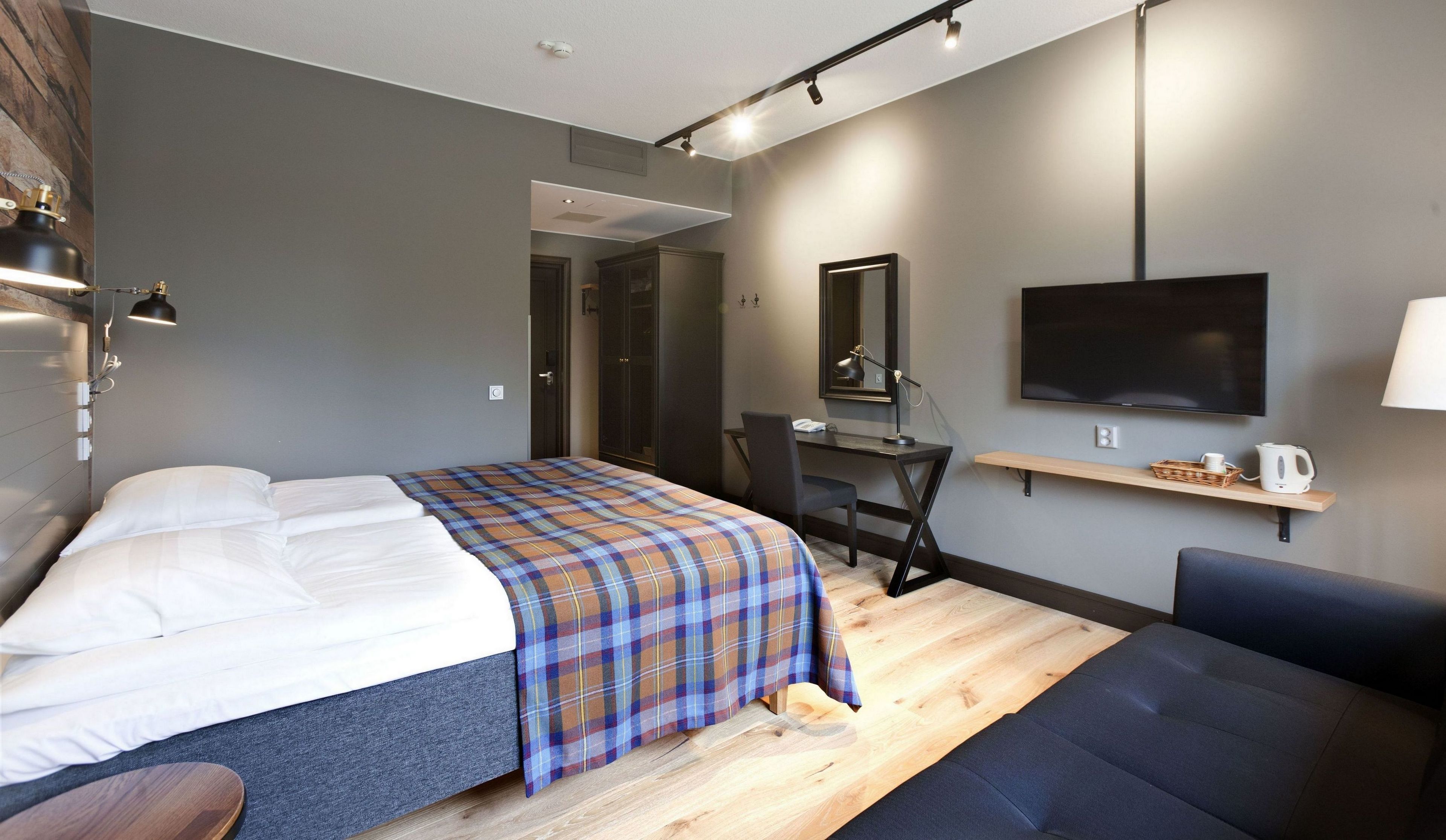 A modern hotel room with a bed, a desk, a chair, a TV, and a sofa.