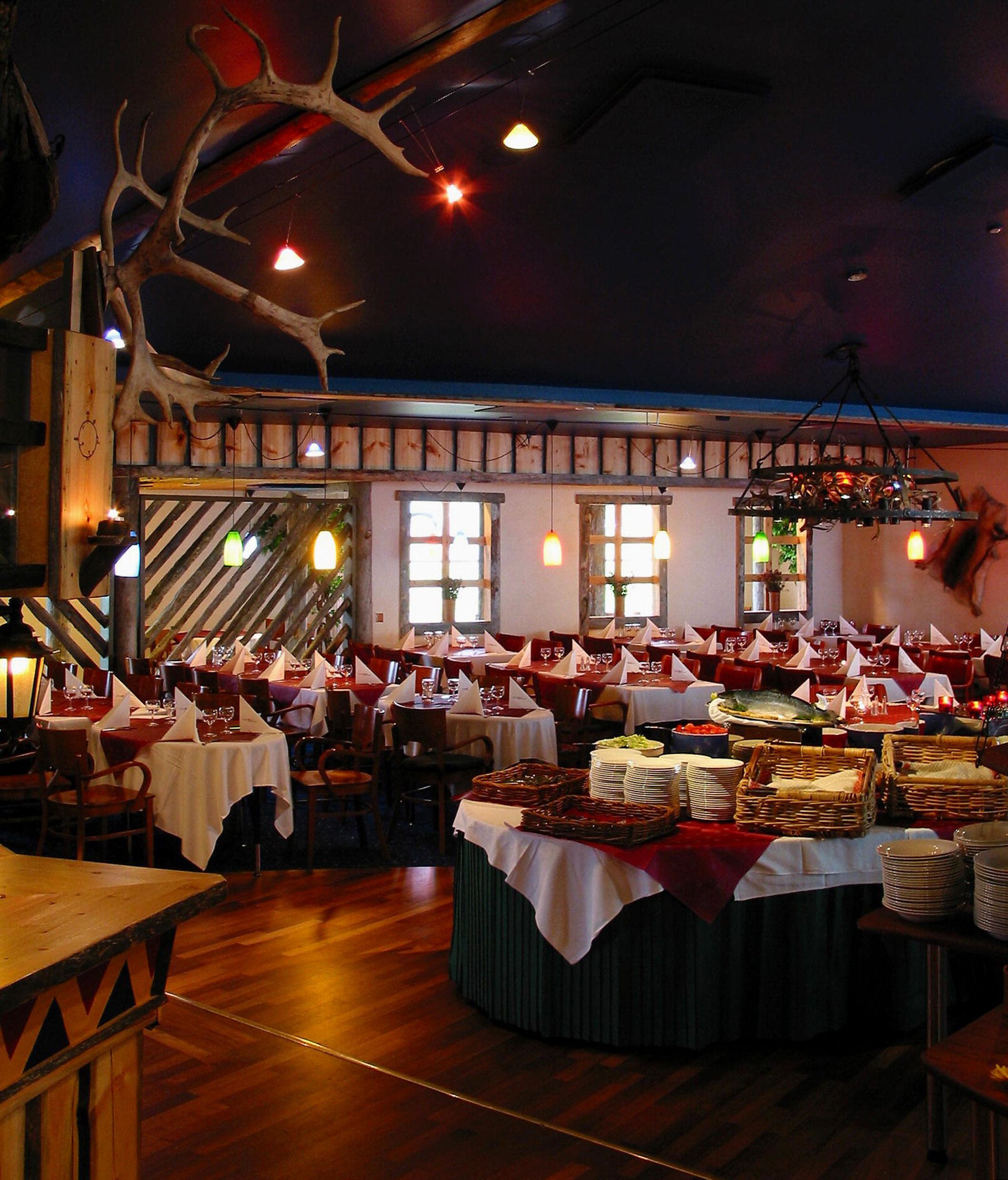 A restaurant with multiple tables set for dining, a central buffet area, and a rustic decor featuring wooden elements and antlers.