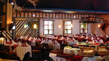 Un restaurante con varias mesas dispuestas para comer, una zona de buffet central y una decoración rústica con elementos de madera y astas.