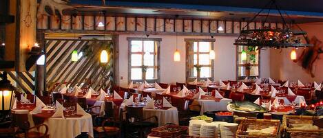 Ein Restaurant mit mehreren Tischen, einem zentralen Buffet und rustikalem Dekor mit Holzelementen und Geweihen.
