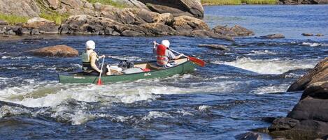 Two people in a green canoe on a river with rocks and greenery in the background.