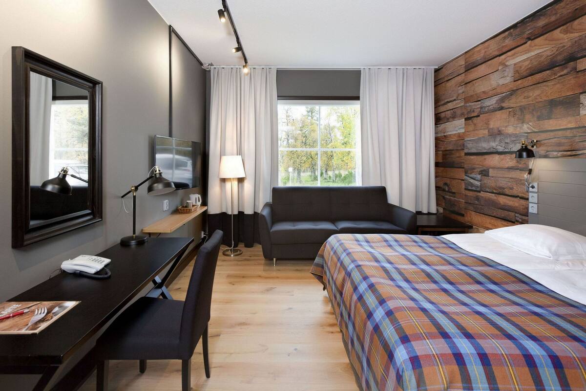 A hotel room with a bed, a desk, a chair, a TV, and a window with curtains.
