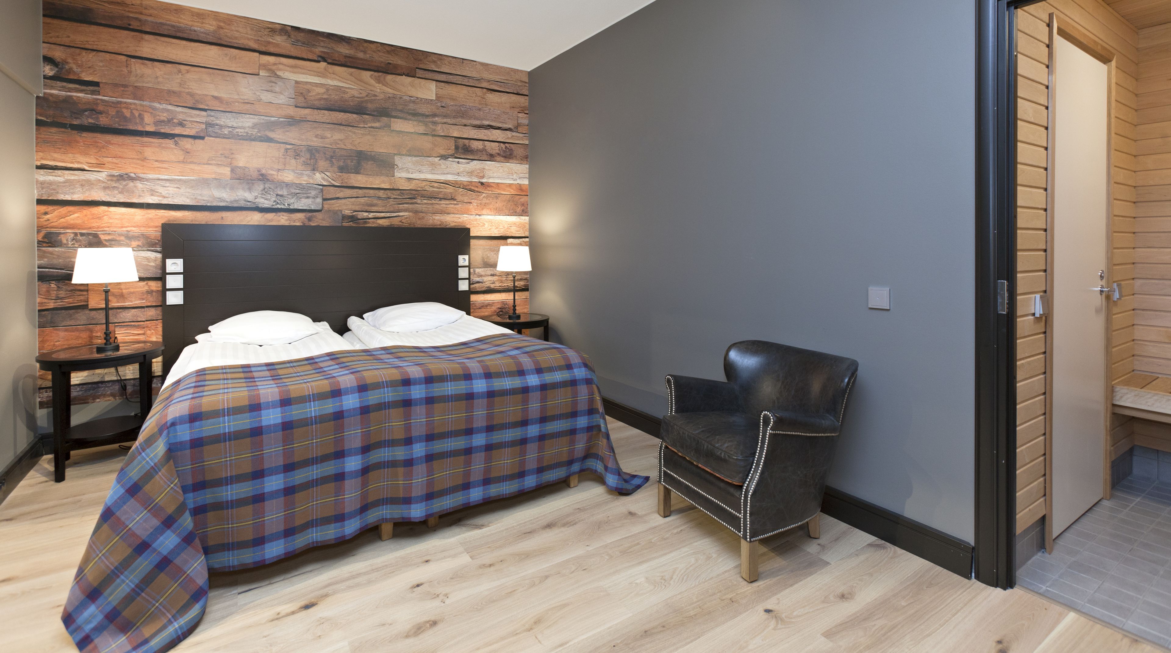 Un dormitorio con una cama, una silla y una mesita de noche con lámparas.