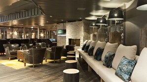 A modern lounge area with leather sofas, wooden tables, and a stone wall.