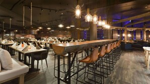 A spacious restaurant with high ceilings, exposed beams, and a long bar area with stools.