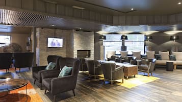 A spacious lounge area with multiple seating options, including sofas and armchairs, a fireplace, and a television screen.