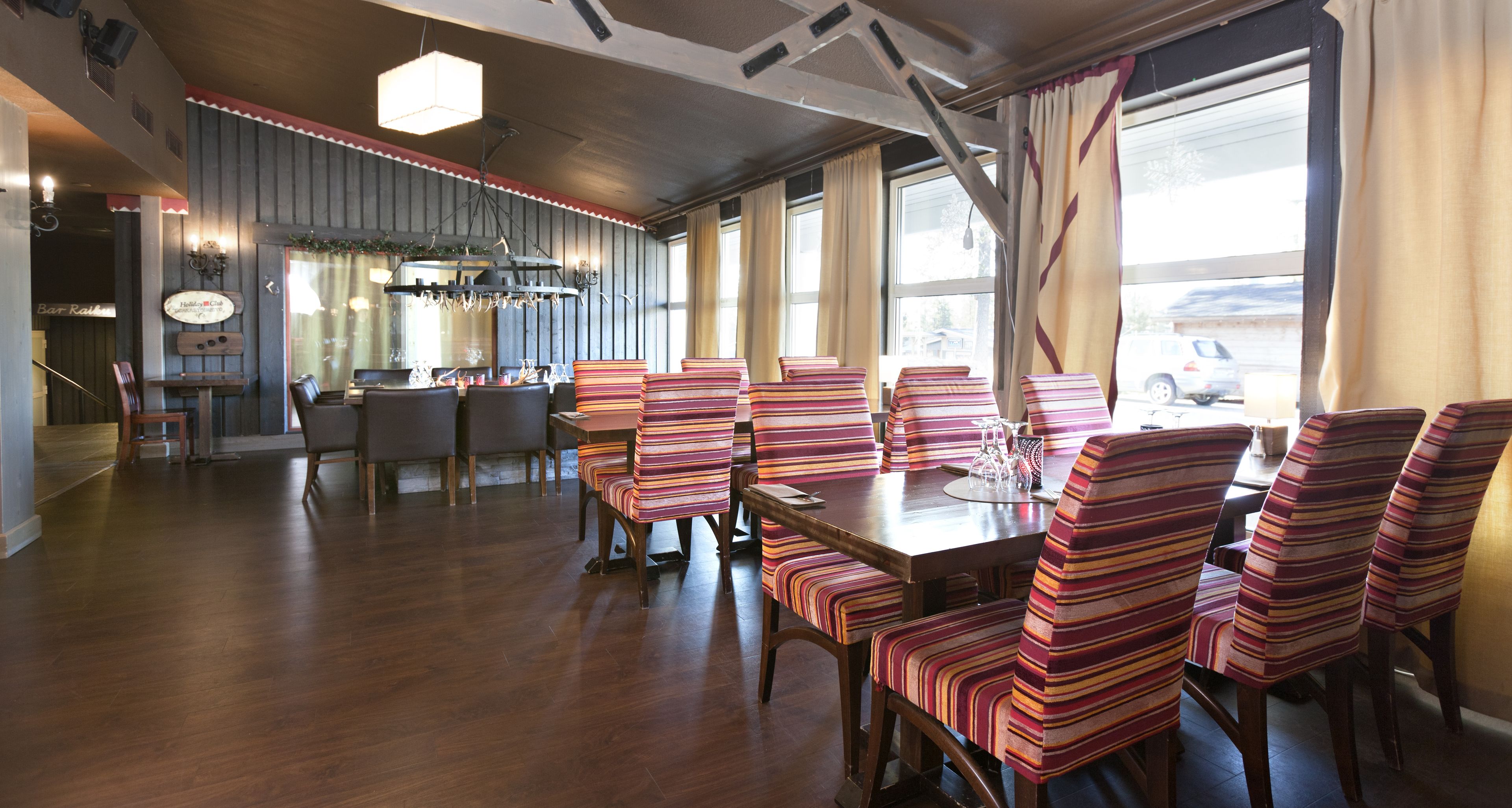 A dining area with striped chairs and a wooden table, large windows, and a bar area in the background.