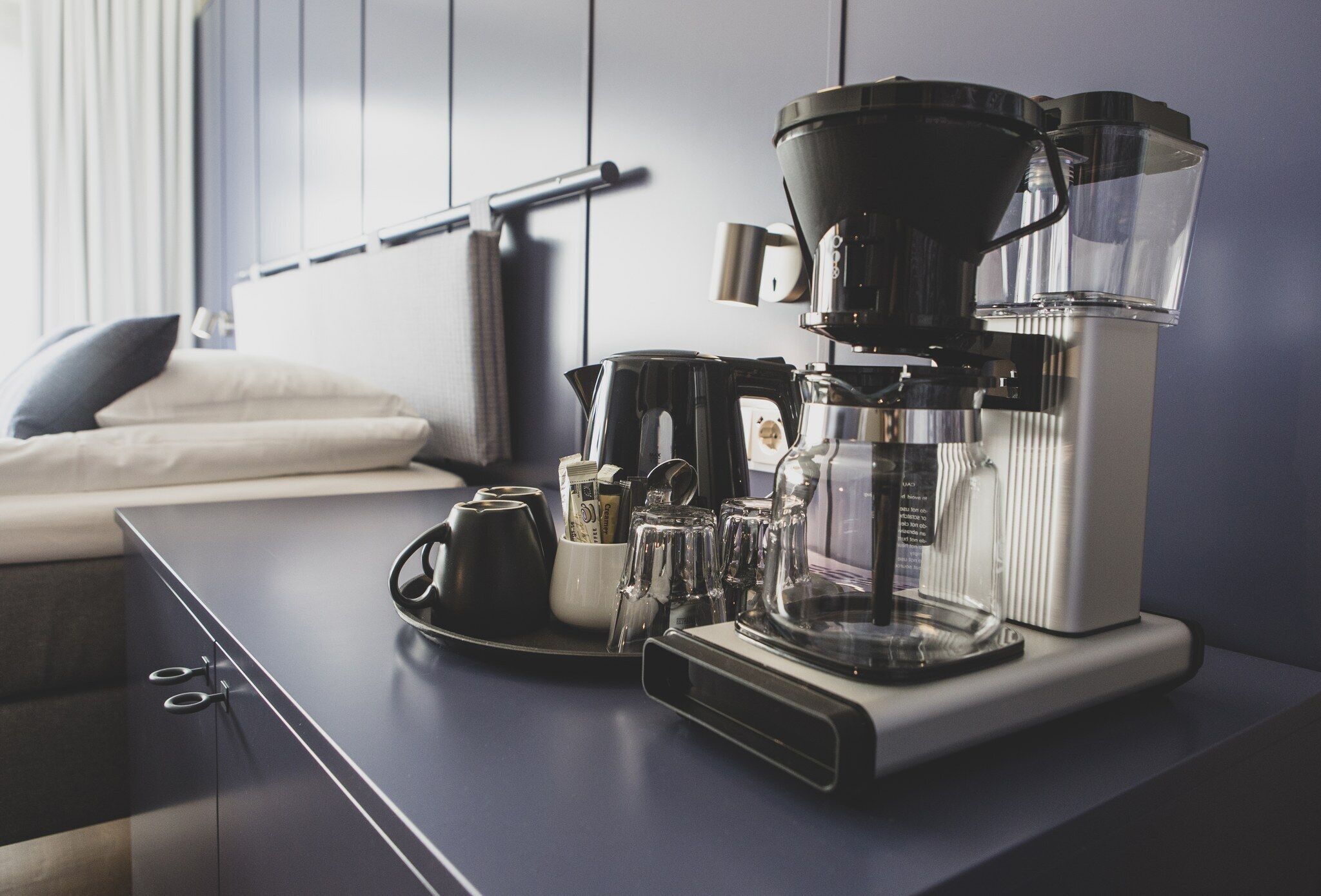 Een koffiezetapparaat op een keukentafel met een waterkoker, kopjes en een koffiemolen.