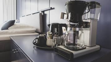 Una cafetera sobre una encimera de cocina, junto a una tetera, tazas y un molinillo de café.