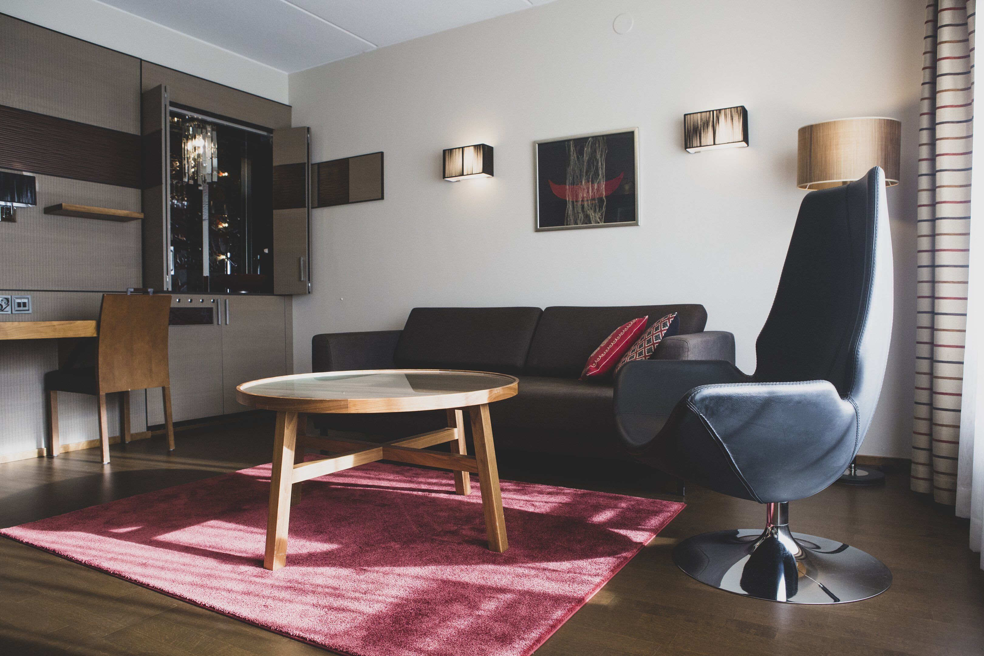 Ein modernes Wohnzimmer mit einem runden Couchtisch, einem schwarzen Sofa, einem blauen Sessel und einem roten Teppich.