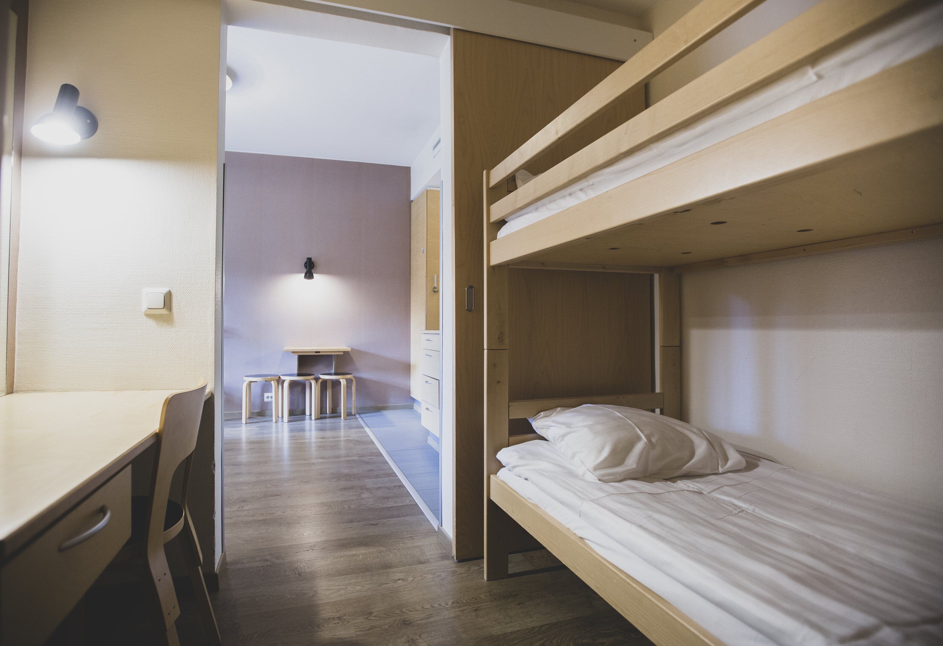 A dormitory room with bunk beds, a desk, and a small table.