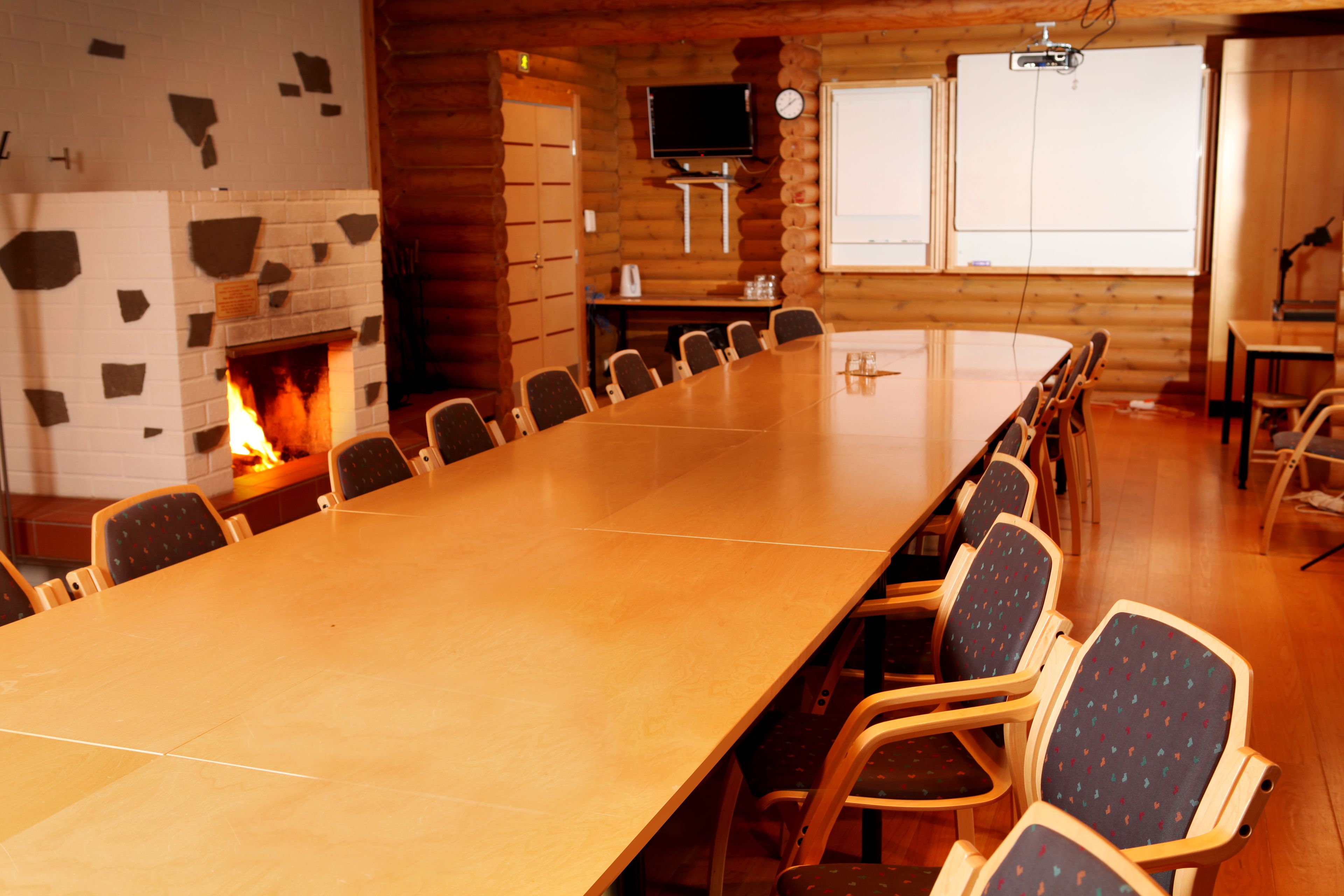 Una sala de conferencias con una larga mesa, sillas, una chimenea, un televisor y una pantalla de proyector.