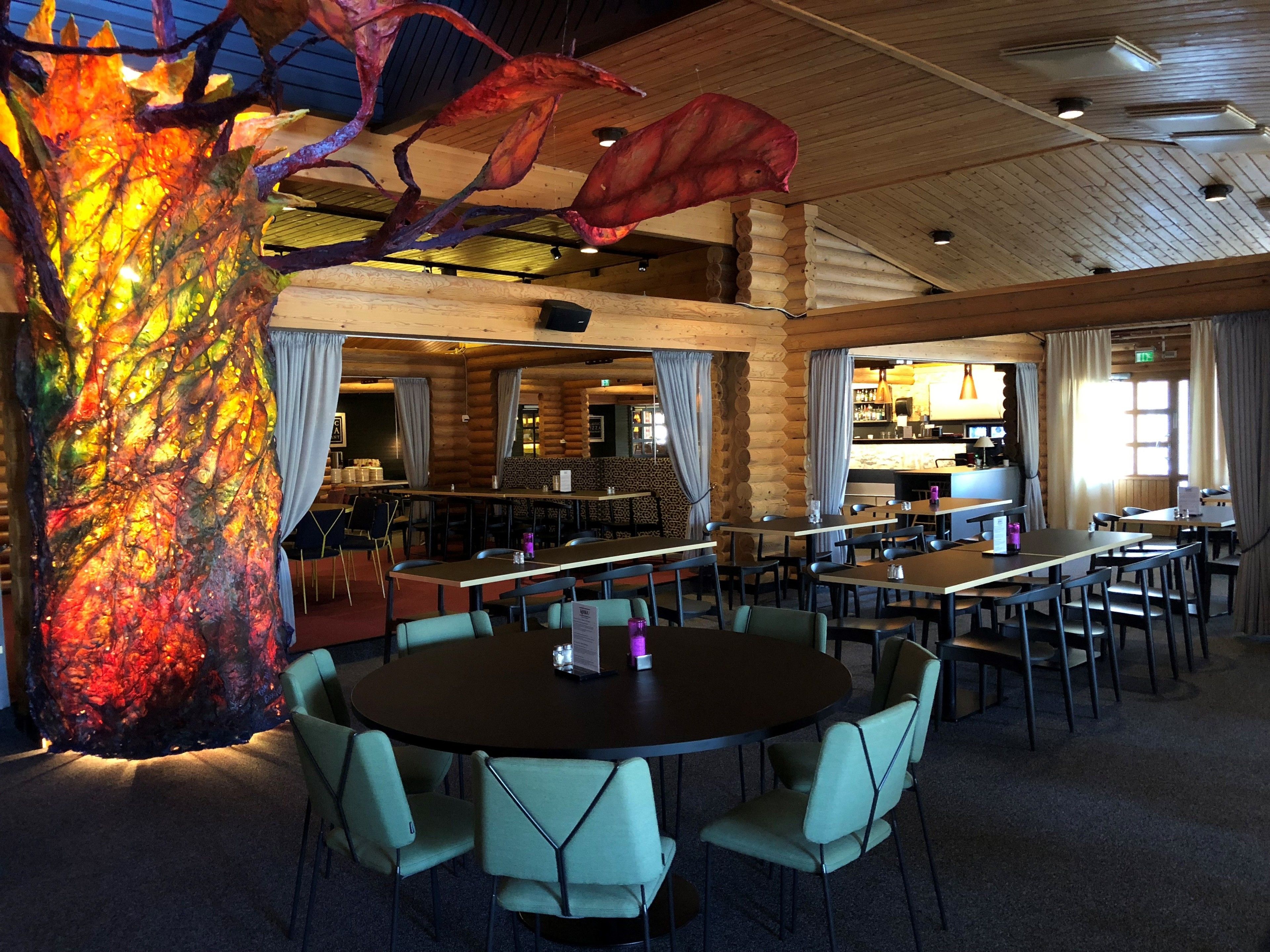 A restaurant with a wooden interior, round tables, and chairs.