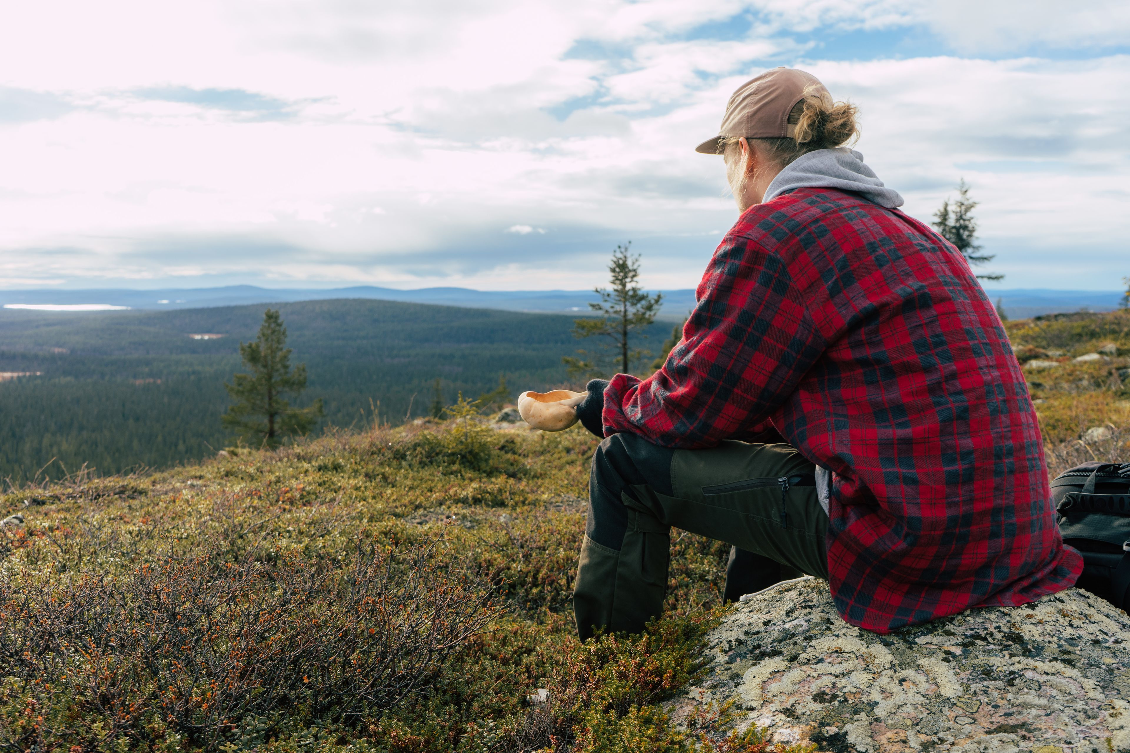 Une personne assise sur un rocher, avec une vue sur un paysage boisé et des montagnes à l’horizon.
