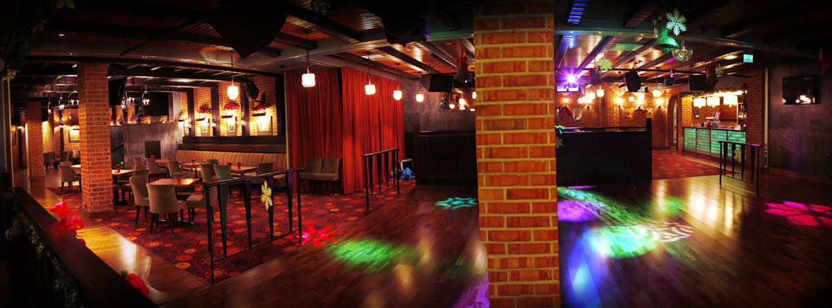 Zona de bar con mesas, sillas y un escenario con cortinas.