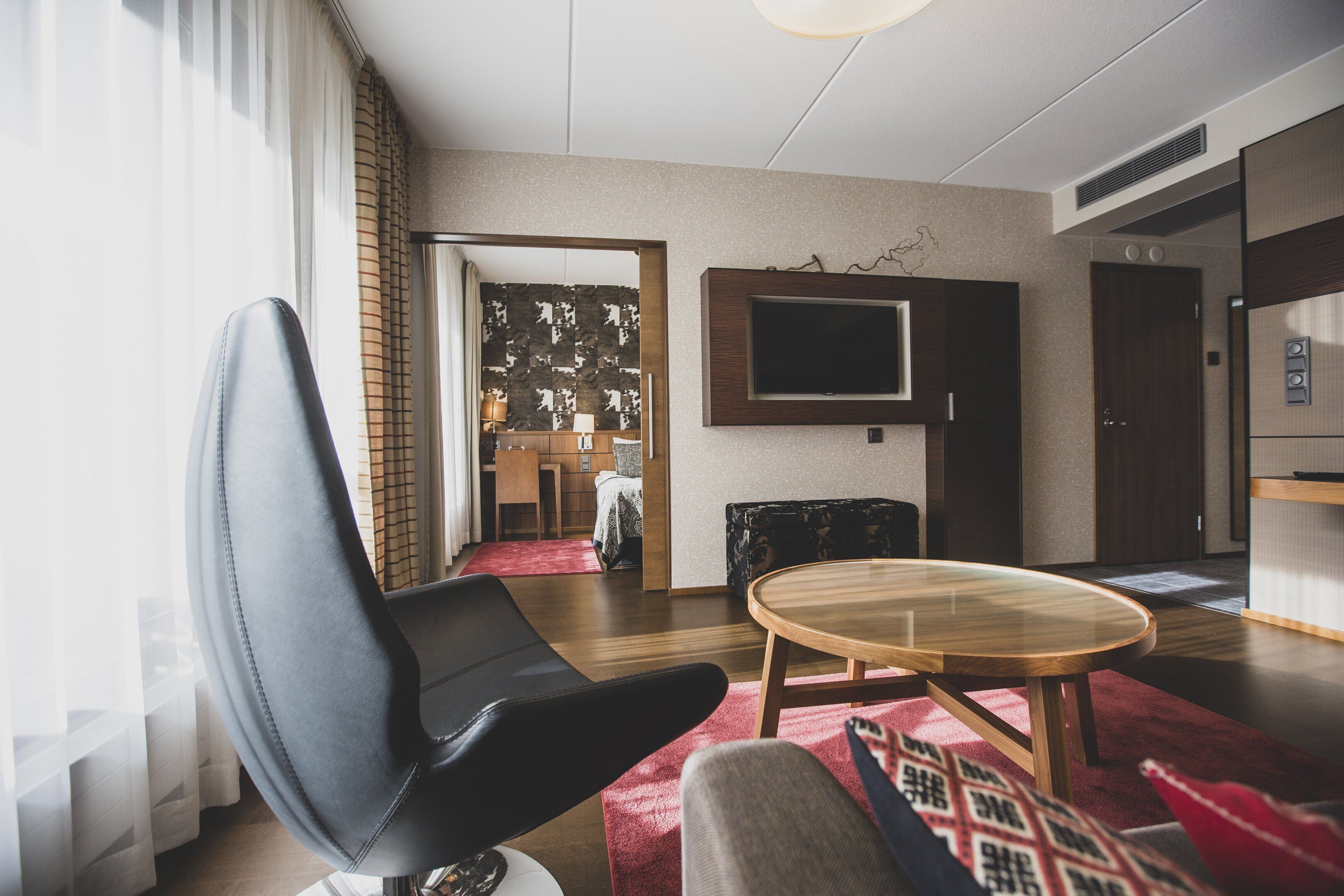 A modern living room with a leather chair, a wooden coffee table, and a flat-screen TV mounted on the wall.