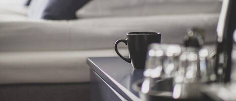 Una cama bien hecha con almohadas, una mesita de noche con una taza negra y un vaso de agua.