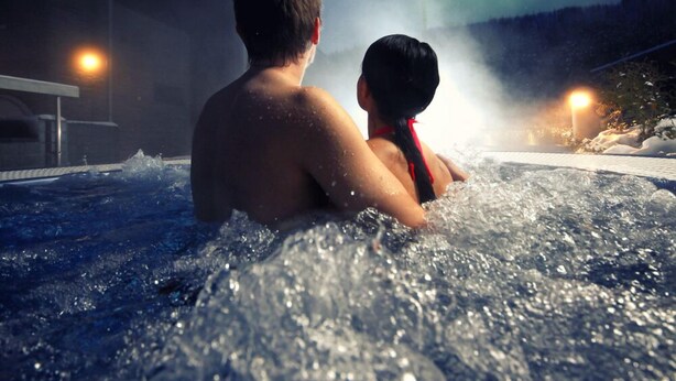 Deux personnes dans un jacuzzi, avec vue sur les aurores boréales.