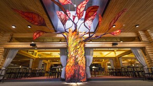 Un grand espace intérieur doté d’une structure arborescente décorative au centre, de murs recouverts de rondins de bois, ainsi que de tables et de chaises disposées pour les repas.