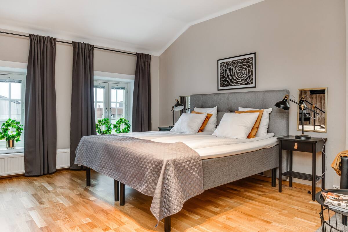 Une chambre à coucher avec un lit, une table de chevet, une lampe et une fenêtre avec des rideaux.
