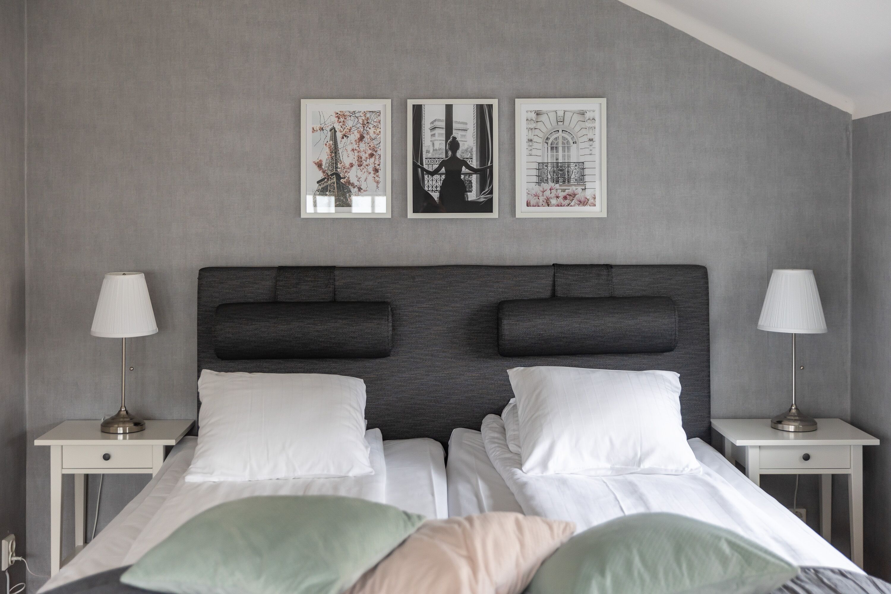 Una habitación de hotel moderna con una cama grande, dos mesitas de noche y tres cuadros enmarcados en la pared.