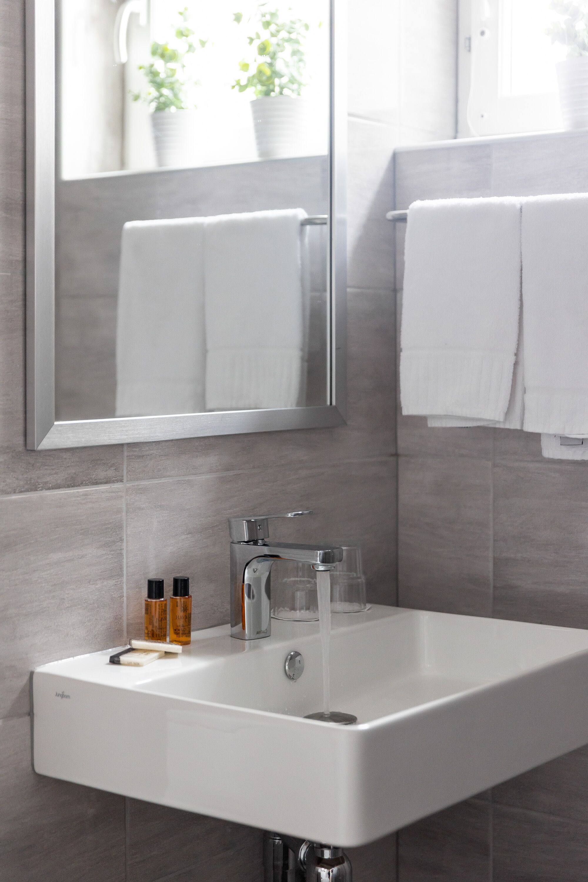 A bathroom with a white sink, a mirror, and a window with potted plants.