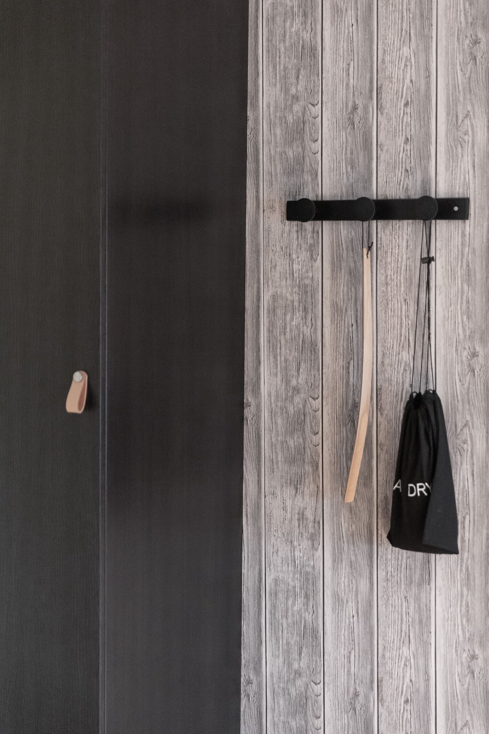 A room with a wooden wall, a black door, and a black bag hanging on a hook.