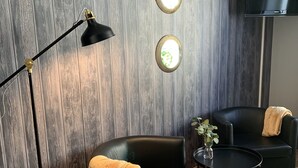 A modern living room with a dark wood-paneled wall, a black leather sofa, a small round table, and a floor lamp. - Ludvika Stadshotell (Ludvika)